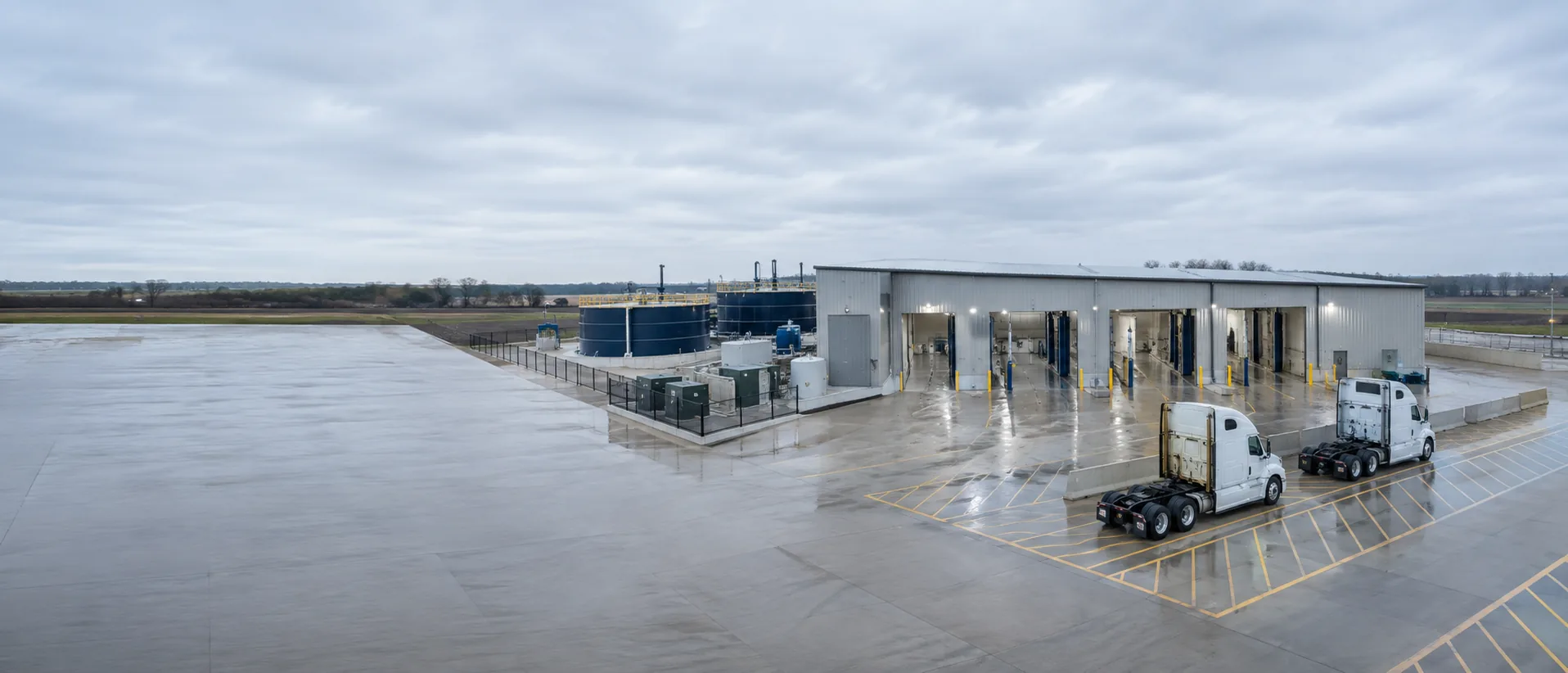 A commercial truck wash facility seen from above, showing the wash bays, the water treatment tanks beside them, and the parking apron.